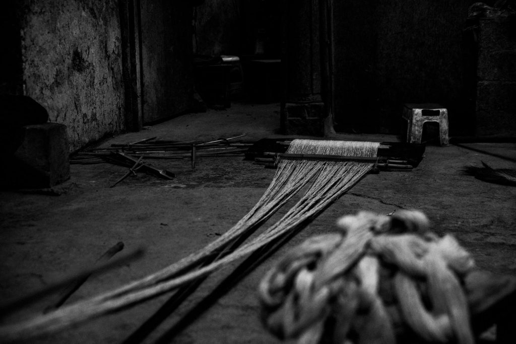 Carbon Fiber Cloth Uses: Stunning Applications in Industry A dramatic black and white photo of industrial weaving equipment featuring ropes and strings.